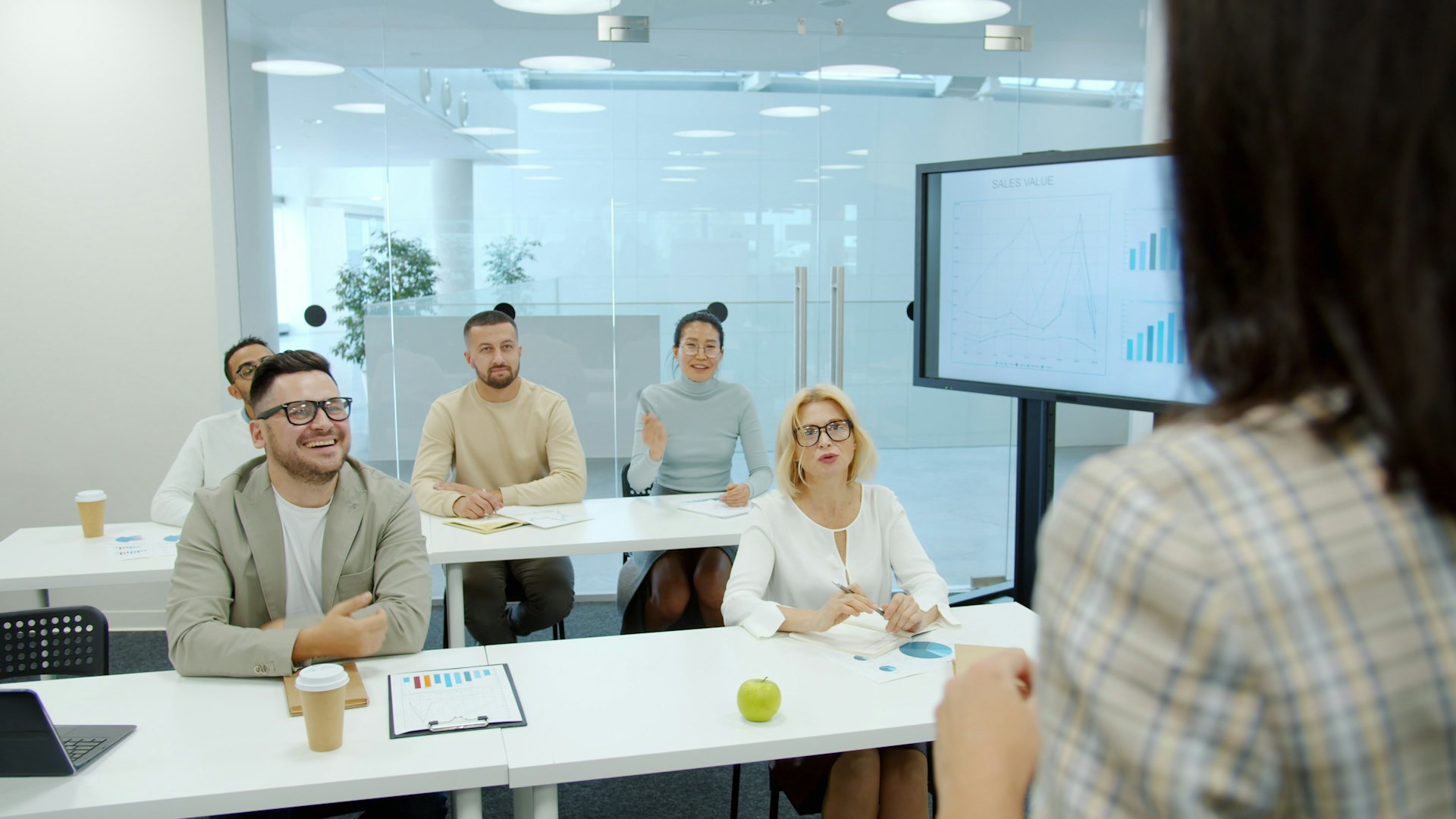 Trainees at desks in a training room listening to an instructor presenting from a screen